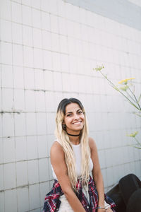 Portrait of young woman sitting against tiled wall