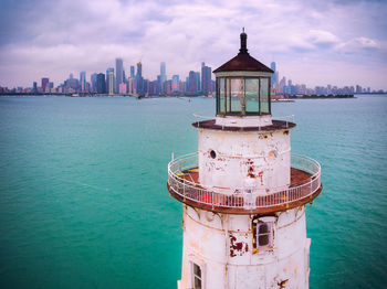 Lighthouse by sea against buildings in city