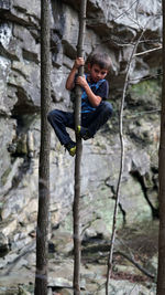 Full length of playful boy climbing on tree against rocks