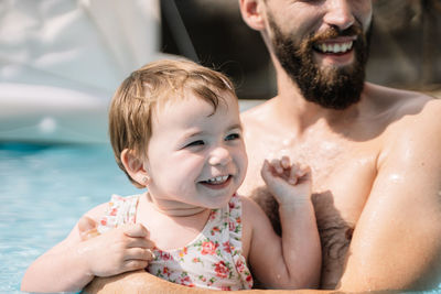 Selective focus on a girl that is smiling while is turning the face in the water embracing a man