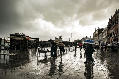 People on wet street against sky during rainy season