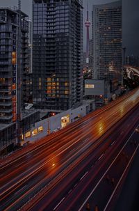 Light trails on road by buildings in city at night