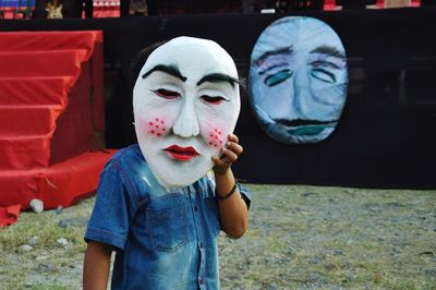 Teenage boy holding big mask while standing against stage