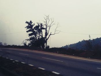 Road by trees against clear sky