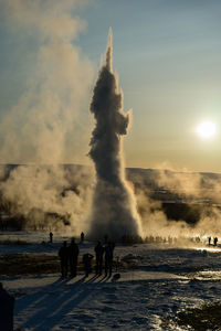 People looking at geyser against sky