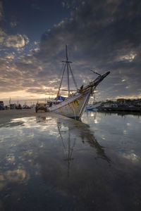 Sailboats moored at harbor against sky during sunset