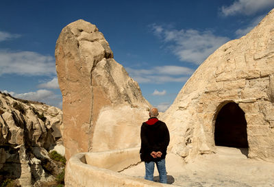 Rear view of woman standing on rock formation against sky