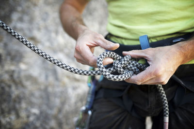 Mid section of man adjusting climbing rope