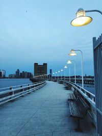 Empty benches on footpath in city against sky at dusk