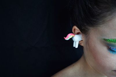 Cropped image of woman with animal figurine in ear against wall