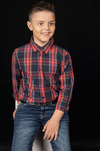 Portrait of boy standing against black background