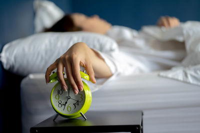 Cropped hand of woman holding alarm clock on bed