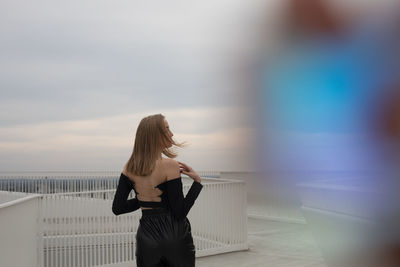 Woman standing by railing against sky