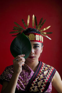 Portrait of young woman holding leaf against red background