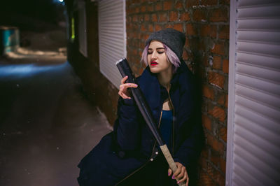 Young woman with baseball bat standing outdoors at night