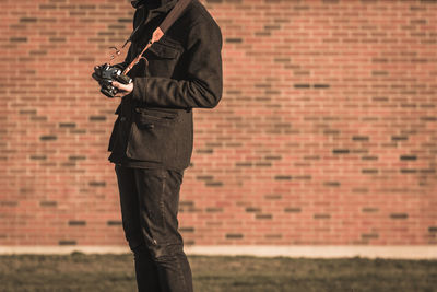 Midsection of man holding camera against wall