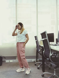 Full length portrait of woman standing against window