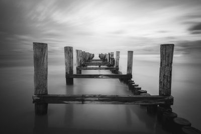 Wooden posts on pier over sea against sky