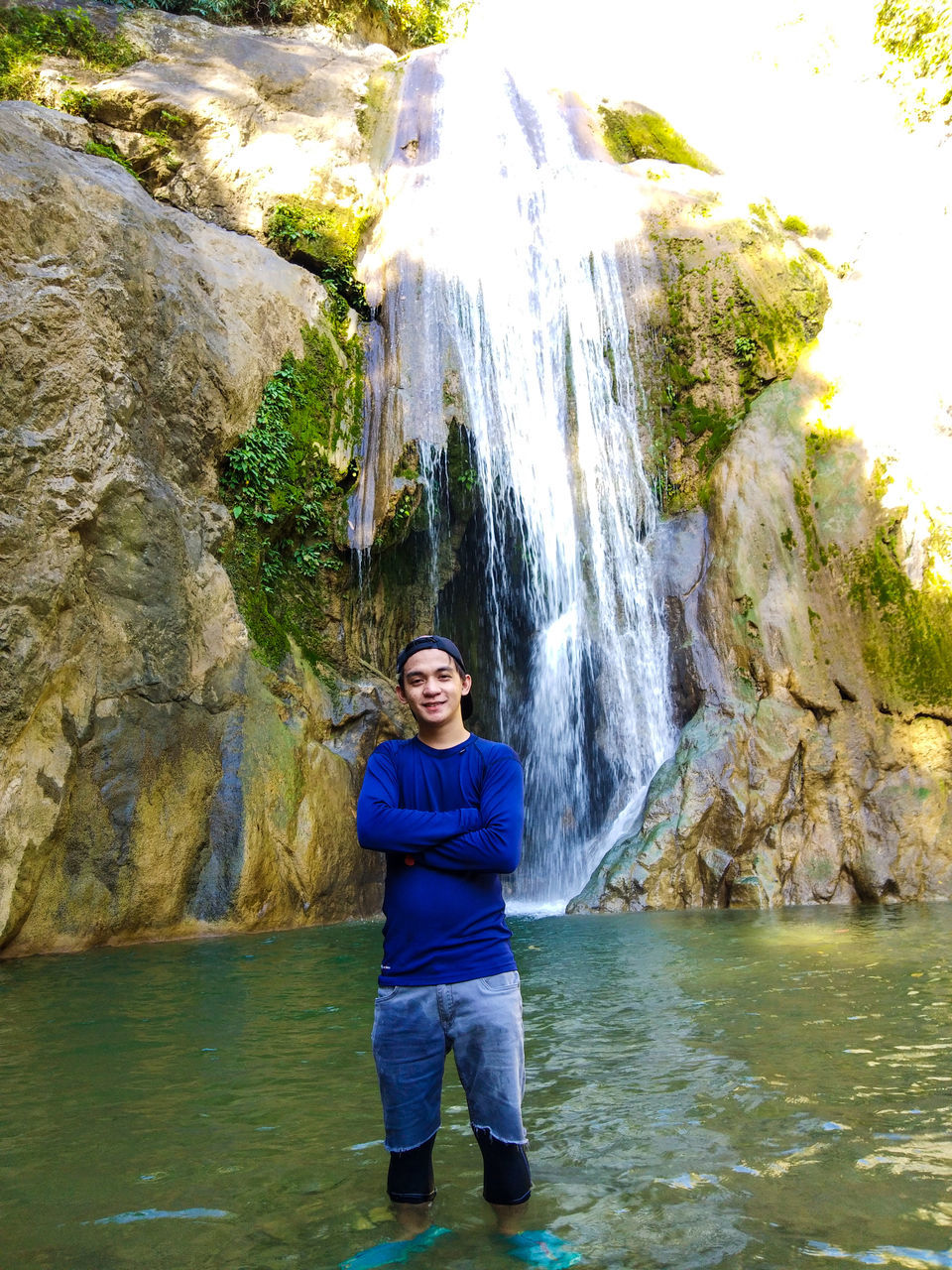 rock - object, water, real people, one person, rock formation, looking at camera, waterfall, portrait, nature, leisure activity, front view, river, day, smiling, outdoors, beauty in nature, waterfront, lifestyles, standing, full length, happiness, scenics, adventure, young adult, young women, people