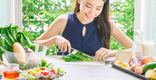 Young woman cutting vegetable on table at home