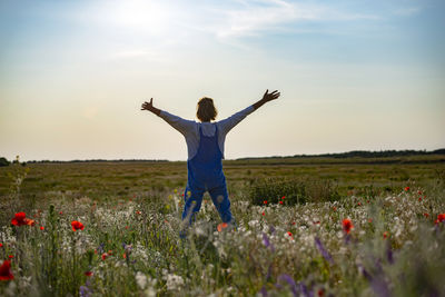 Rear view of woman with arms outstretched standing on field against sky