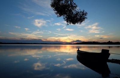 Silhouette boat moored at lake against sky during sunset