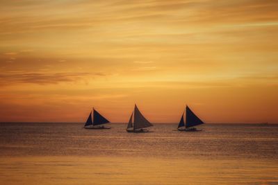 Sailboat sailing on sea against orange sky