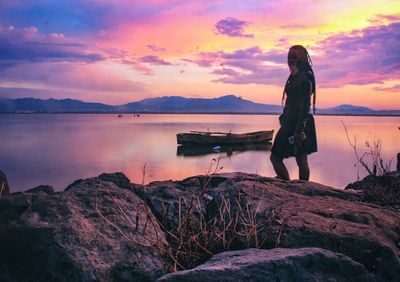 Man standing on rock against sky during sunset