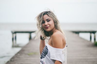 Beautiful young woman on pier at beach against sky