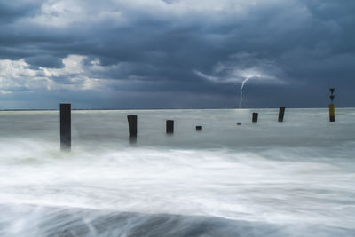 Wooden posts in sea against sky