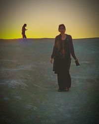 Young couple standing on land against sky during sunset