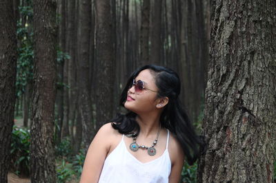 Smiling young woman wearing sunglasses while tossing hair at forest