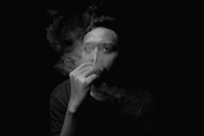 Portrait of man smoking cigarette against black background