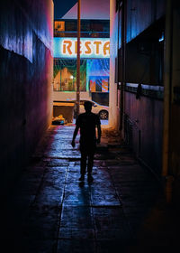 Rear view of man walking on footpath amidst buildings in city