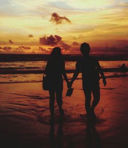 Rear view of silhouette friends walking on beach during sunset