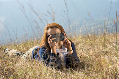 Full length of woman photographing while lying down on grassy field