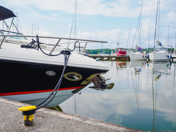 Close up view on bow of moored motorboat on quayside with jetty ful of sailing yachts on background