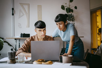 Young male freelancer explaining female colleague while discussing over laptop at home office