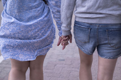 Midsection of women holding hands while walking on footpath