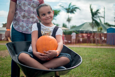 Portrait of cute girl with pumpkin on grass
