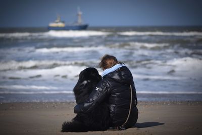 Rear view of woman with dog on beach against sky