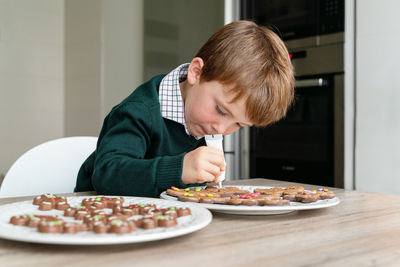 Cute boy decorating gingerbread cookies at home