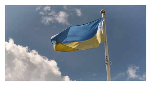 Ukrainian flag flying from mast blown by the wind against pale blue sky and clouds 
