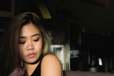 Thoughtful young woman looking down while sitting at home