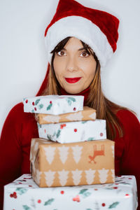 Portrait of smiling woman holding christmas gifts while standing against white background