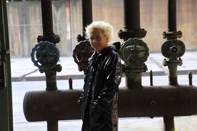 Smiling mature woman standing by pipes