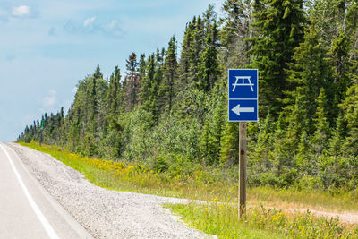 Road sign by trees against sky