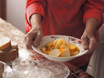 An elderly woman in brightly colored clothes sets the table, holds, and offers homemade diet potato 