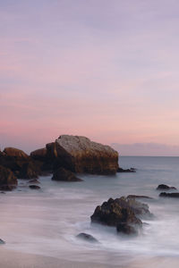 Rocks in sea against sky during sunset