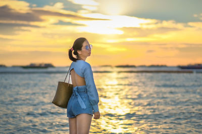 Woman standing on beach against sky during sunset